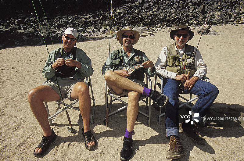 三个男人坐在户外，拿着飞钓装备，面带微笑的肖像图片素材