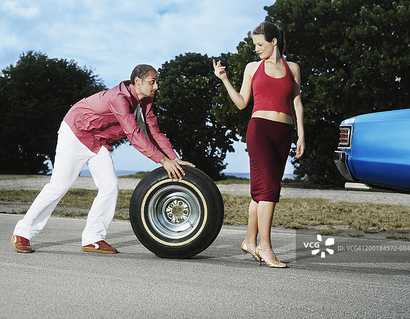 男子滚动轮胎，跟随招手的女子图片素材