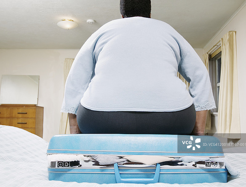 坐在手提箱上的中年妇女，后视图图片素材