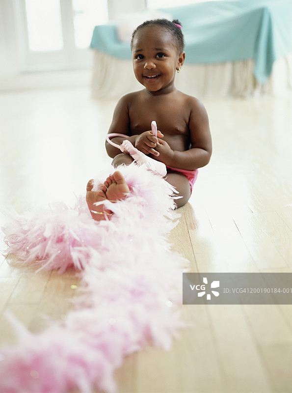 地板上拿着羽毛围巾微笑的女童（1-3岁）肖像图片素材