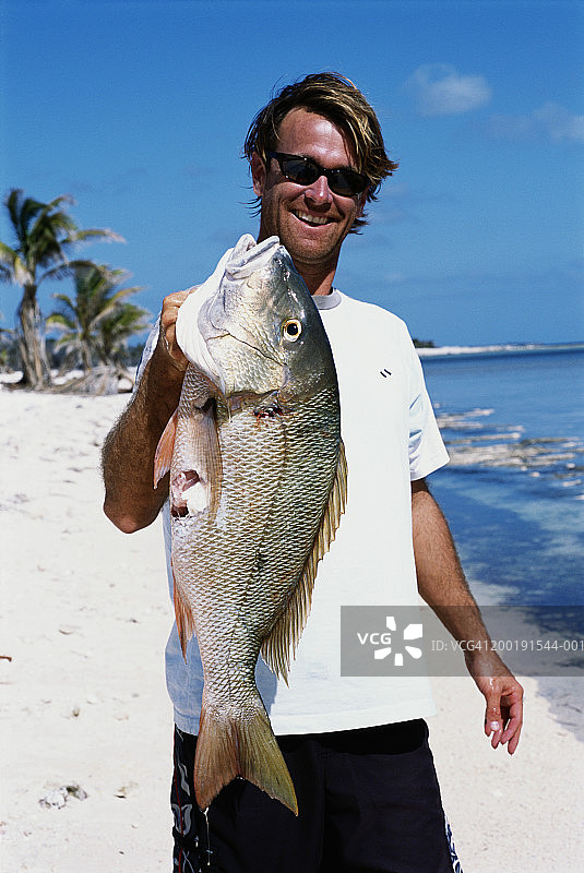 男人在海滩上手持叉住的鲷鱼图片素材