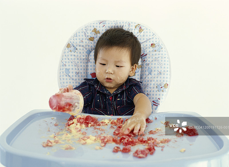 坐在高脚椅上玩甜点的男婴（12-15个月）图片素材