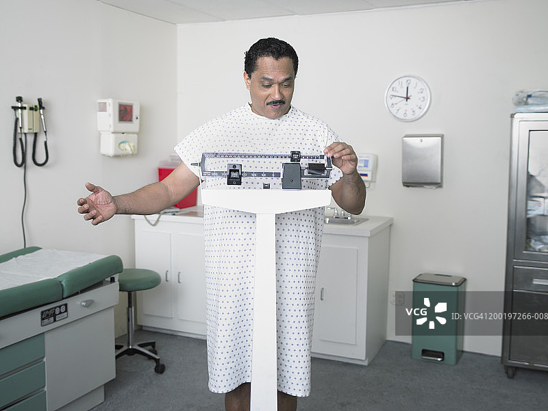 在检查室里站在体重秤上微笑的中年男人图片素材