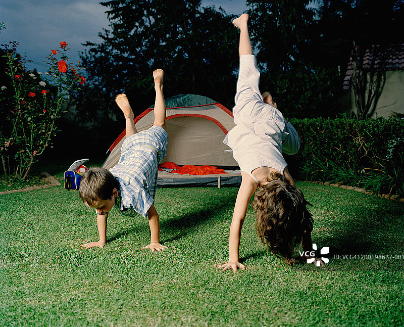 男孩和女孩(6-8岁)在帐篷旁的草地上表演倒立图片素材