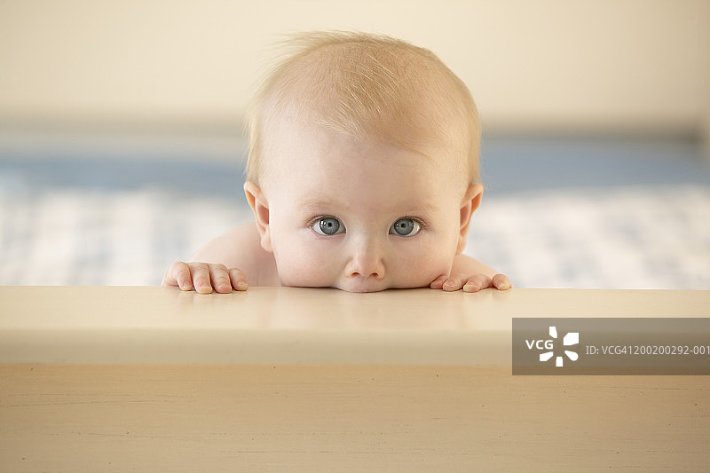 男婴（6-9个月）咬着婴儿床边缘，肖像图片素材