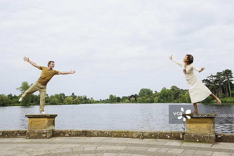 年轻情侣在湖边矮墙上保持平衡图片素材