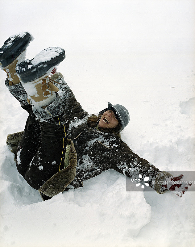 女人躺在雪地里，双腿朝上，笑着图片素材