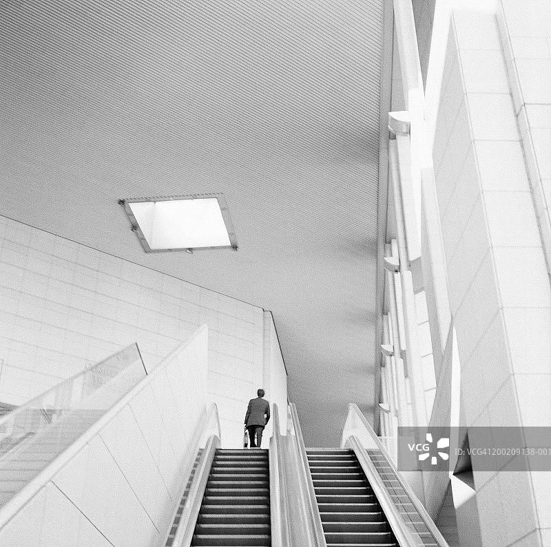 在自动扶梯上的商人，后视图，低角度视图（颗粒状黑白照片）图片素材