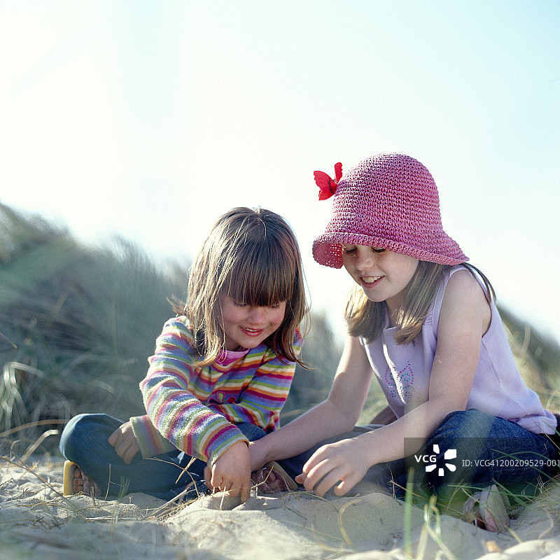 在沙滩上玩沙的两个姐妹（6-9岁），面带微笑图片素材