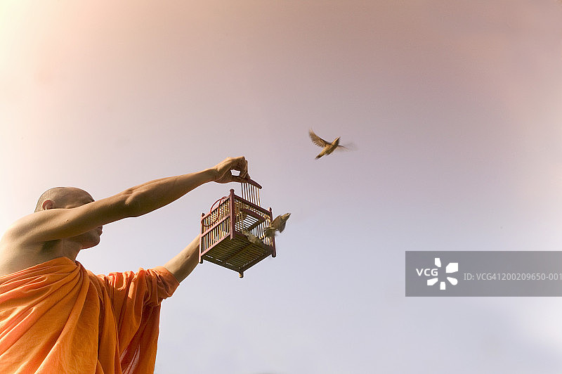 佛教僧侣放生笼中鸟，低角度拍摄图片素材