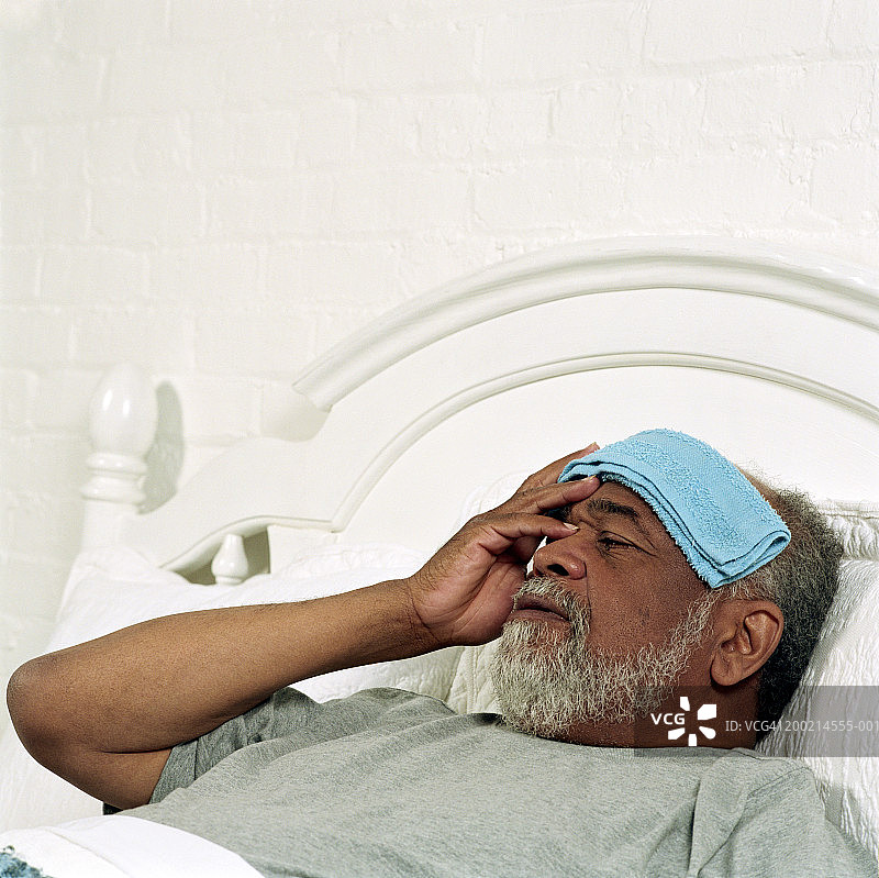 年长的男人躺在床上，手拿法兰绒按着额头，特写镜头图片素材
