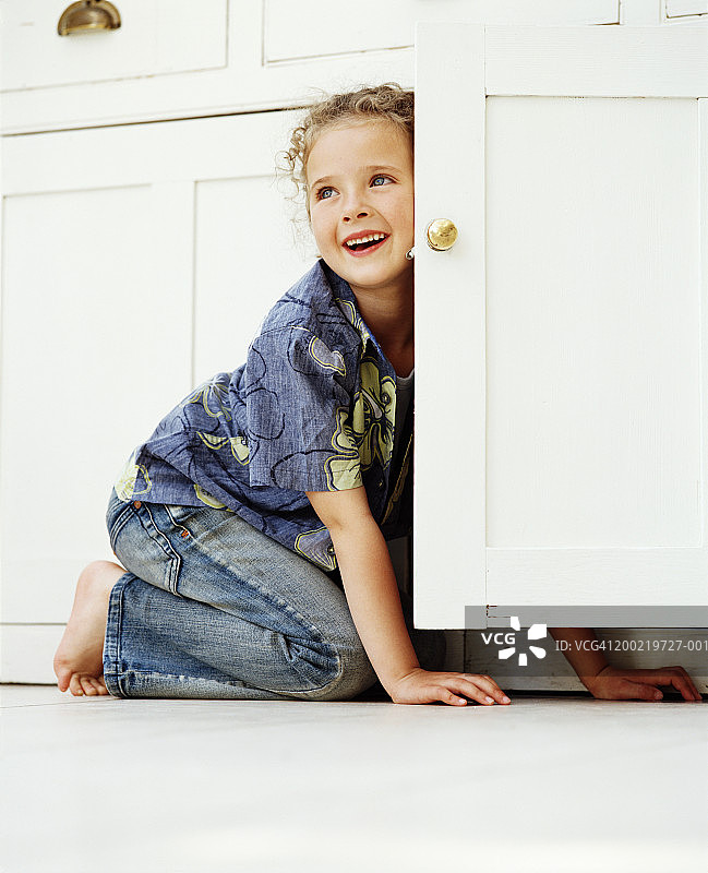跪在打开的橱柜旁，微笑的女孩图片素材