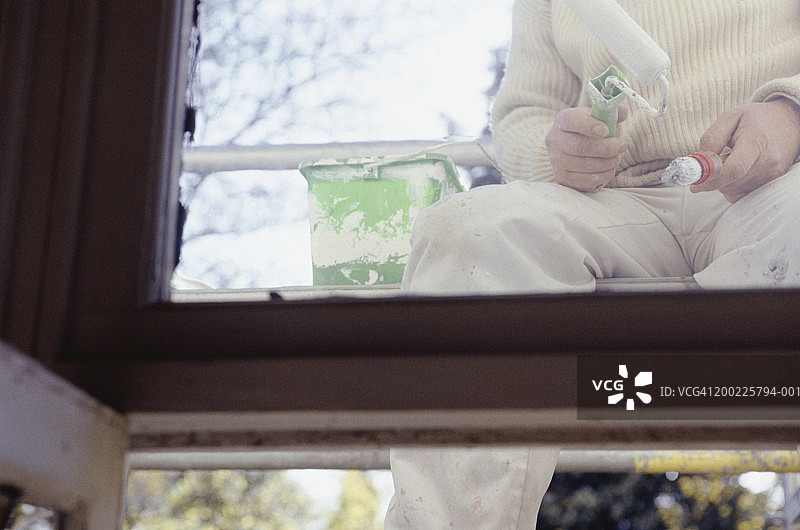 工人坐在脚手架上，手持画笔和油漆滚筒（中段）图片素材