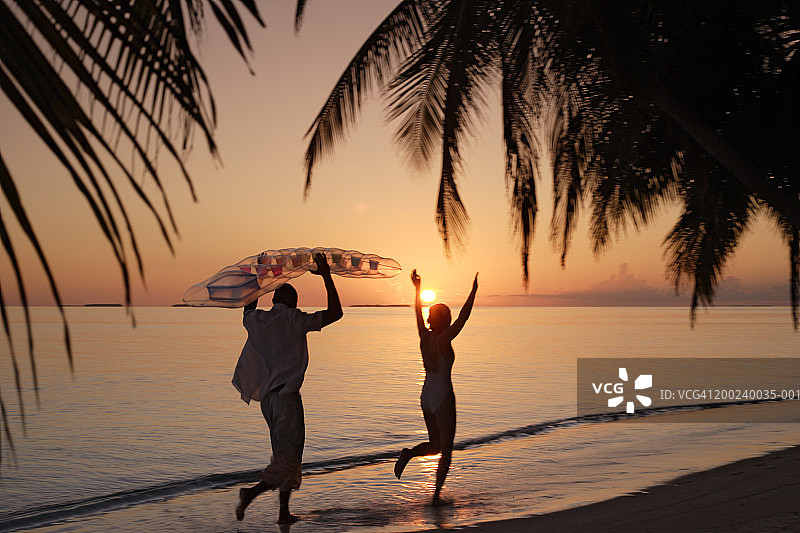 情侣在海滩奔跑，男人拿着充气筏，日落时分图片素材