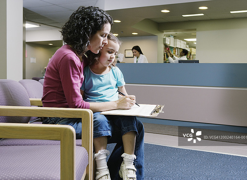 女人在医疗中心填写表格，3-5岁的女孩坐在腿上图片素材