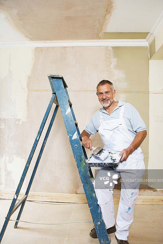 梯子旁手持油漆刷和托盘的中年男人肖像图片素材