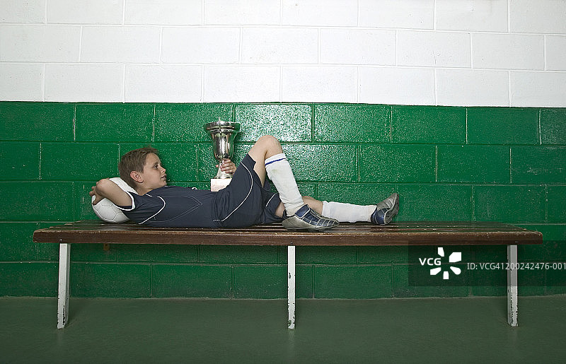 躺在更衣室长椅上，手持奖杯的男孩（8-10岁）图片素材