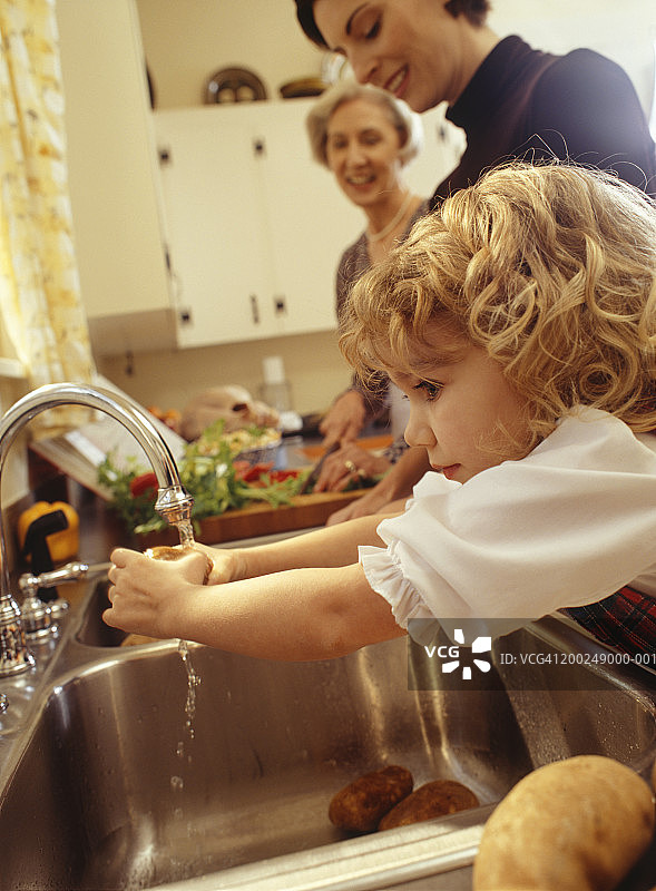 孙女（4-5岁）与母亲和祖母在水槽里洗土豆图片素材