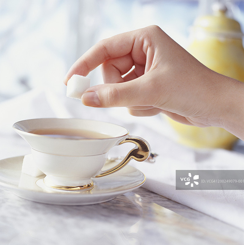 女人在茶杯里放糖块，手部特写图片素材