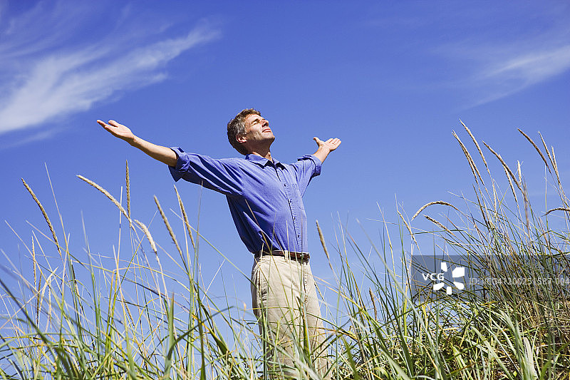 中年男人站在田野里，双臂伸展，闭着眼睛图片素材