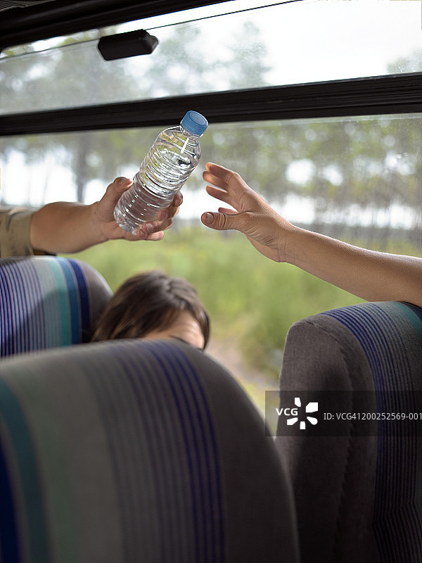 青年男子在长途汽车上递水给年轻女子图片素材