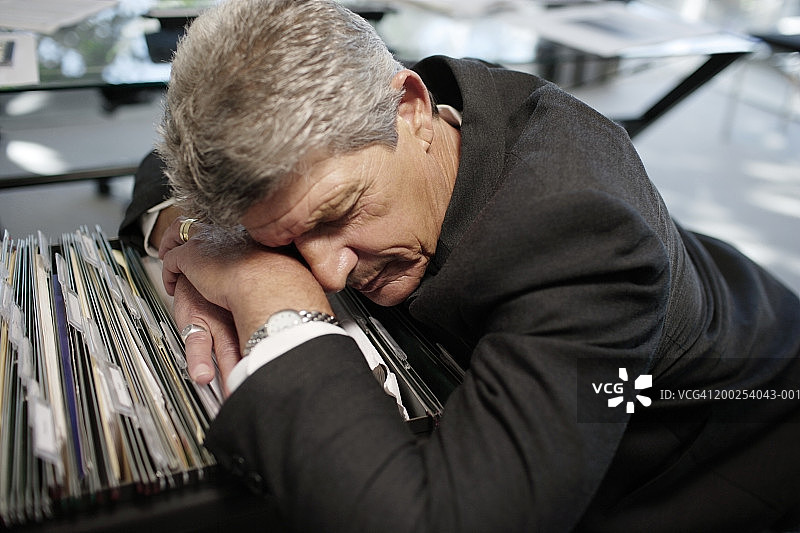 在文件柜抽屉上睡着的中年商人，特写镜头图片素材