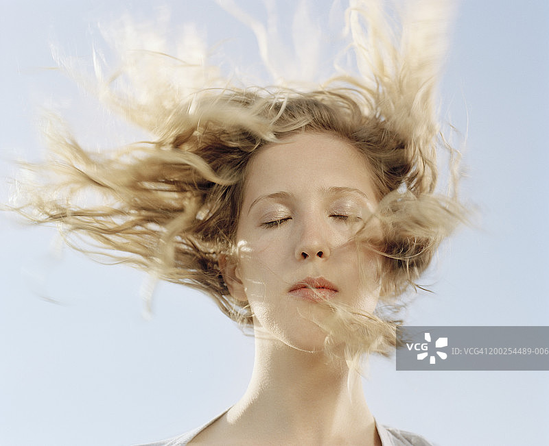 闭着眼睛，面部吹着头发的年轻女人特写图片素材