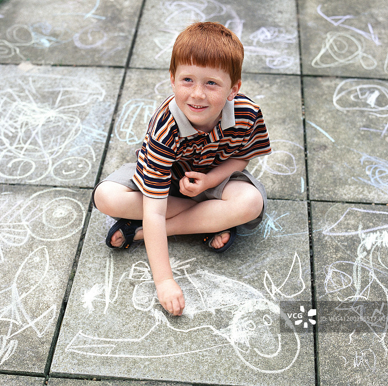 男孩（4-6岁）在石板路上用粉笔画画，面带笑容，俯视图片素材