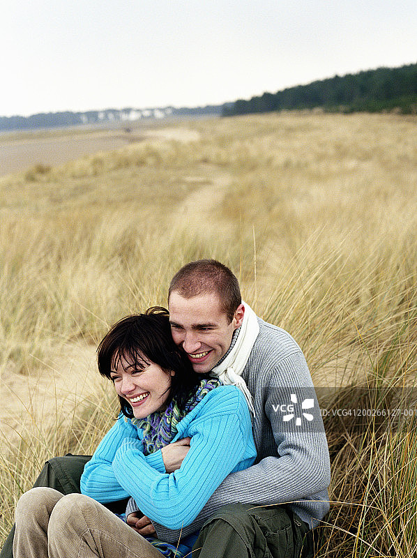 年轻情侣坐在草地沙丘上，开怀大笑图片素材