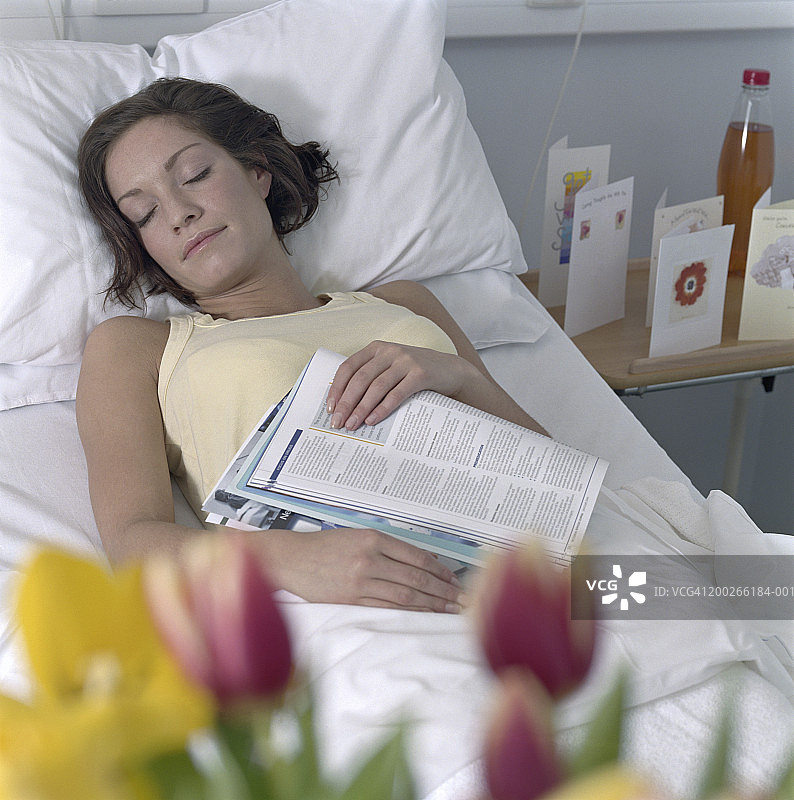 女病人睡在医院的病床上，胸前放着杂志图片素材