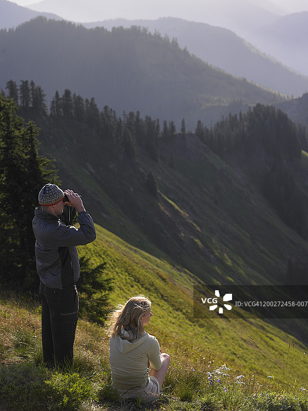 山中的年轻夫妇，男人正在用双筒望远镜观察图片素材