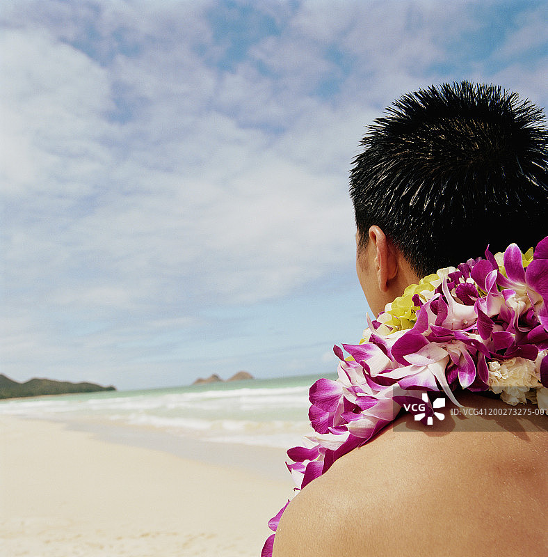戴着花环的年轻男人在海滩上向下看，特写，后视图图片素材