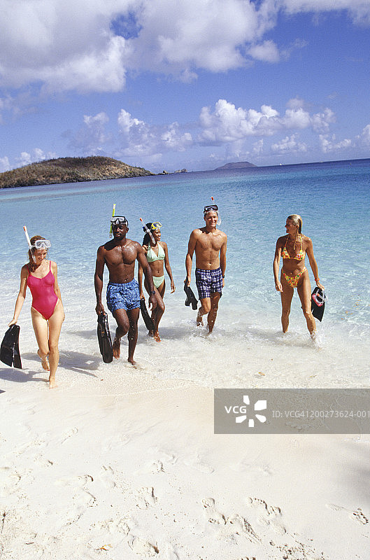 一群朋友在海滩上行走，携带浮潜设备图片素材