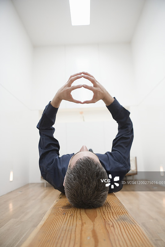 男人躺在长椅上，抬起手臂，指尖合拢图片素材