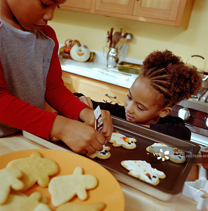6-8岁女孩看着4-6岁的男孩在厨房里给姜饼人上糖霜图片素材