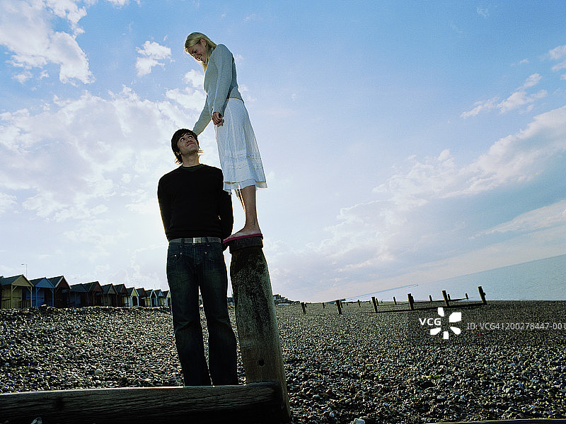 在卵石滩上，男人抬头看着站在防波堤上的女人图片素材