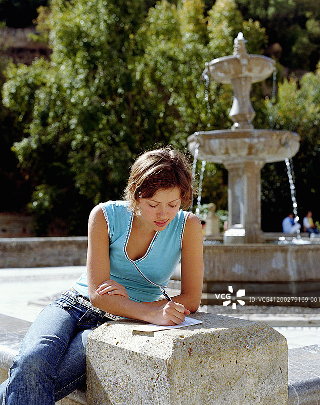 年轻女人坐在喷泉旁写信图片素材