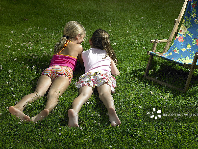 两个女孩（4-6岁）躺在草地上聊天，后视图图片素材
