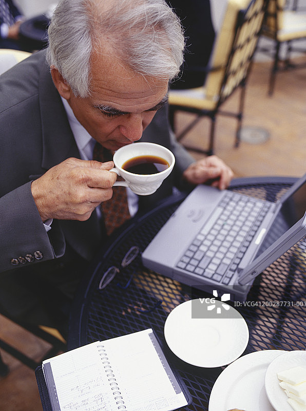 在户外咖啡馆喝咖啡的笔记本电脑商人图片素材