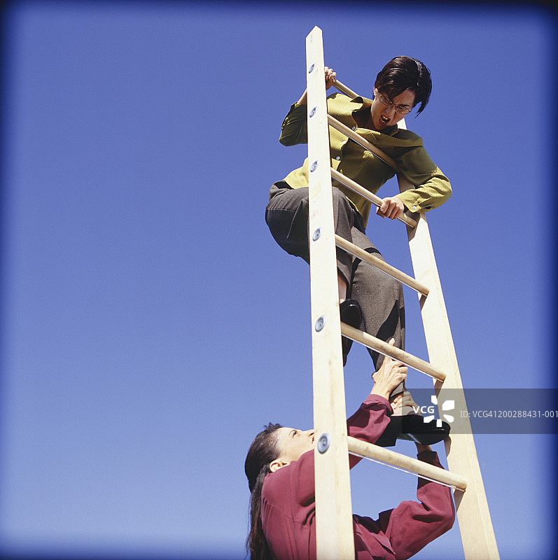 低角度看商务女人试图将对手从梯子上拉下来图片素材