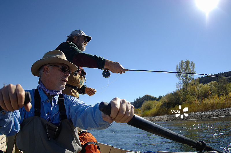 两个男人在河上的船上，一个男人在飞蝇钓鱼，低角度视角图片素材