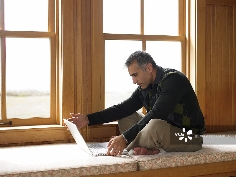 男子坐在窗边座位上使用笔记本电脑，侧视图图片素材