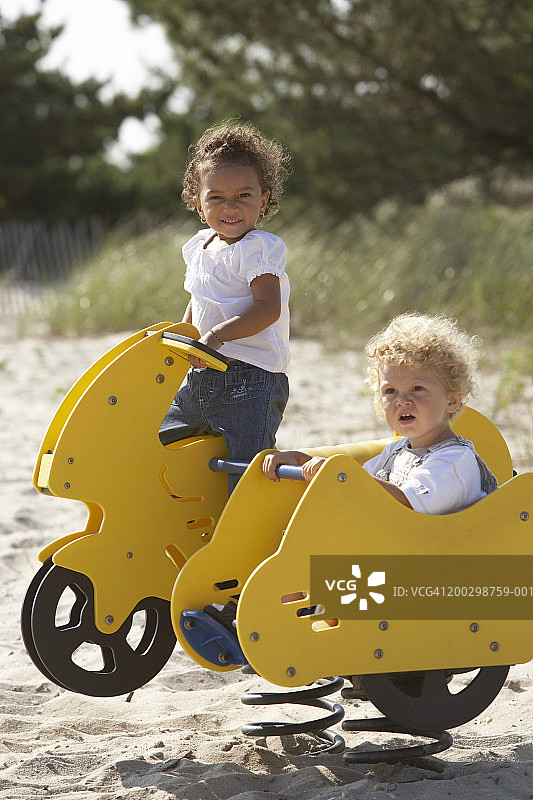 在游乐场摩托车和挎斗上玩耍的幼儿男孩和女孩（2-4岁）图片素材