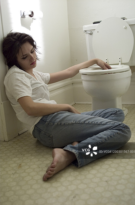生病的年轻女人靠着浴室墙壁图片素材