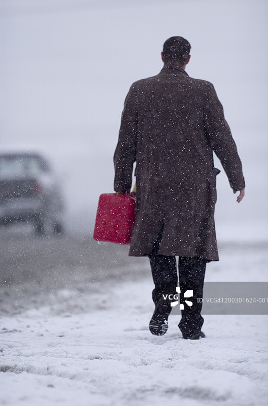 商人在雪地道路旁持汽油桶行走图片素材
