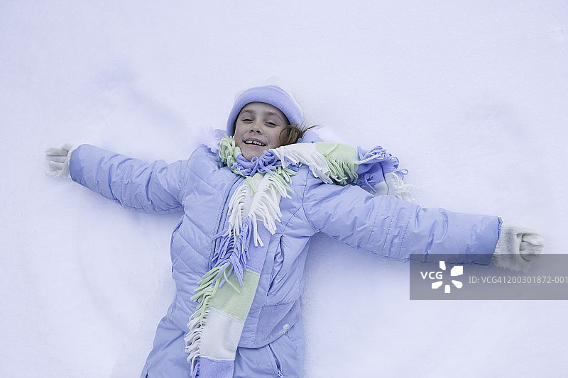 年轻女孩（6-7岁）躺在雪地上，用身体做出天使的形状，肖像图片素材