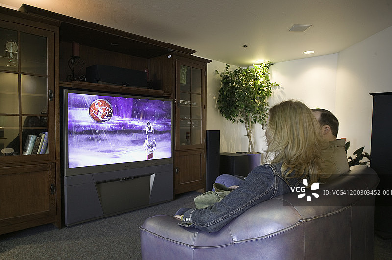 夫妻在书柜前看宽屏电视。图片素材