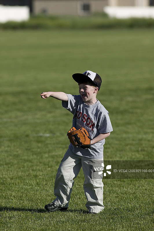 男孩（6-7岁）戴着棒球手套站在田野里，指向前方图片素材