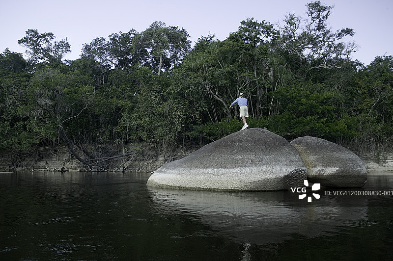 男人站在水中巨大的光滑岩石上图片素材