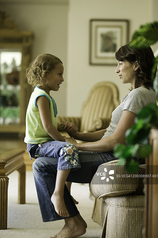 小女孩（6-7岁）坐在母亲的腿上，在客厅里图片素材